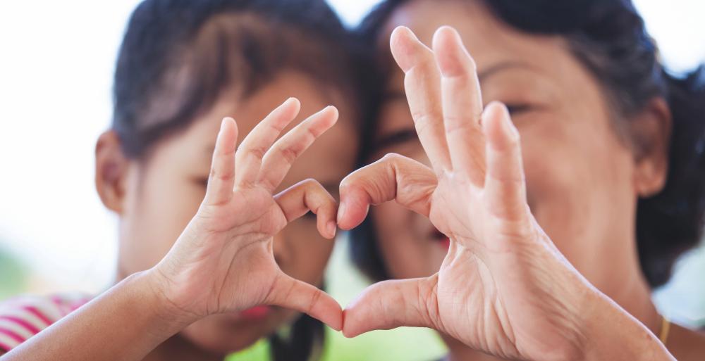 A mom and daughter making a heart shape with their hands